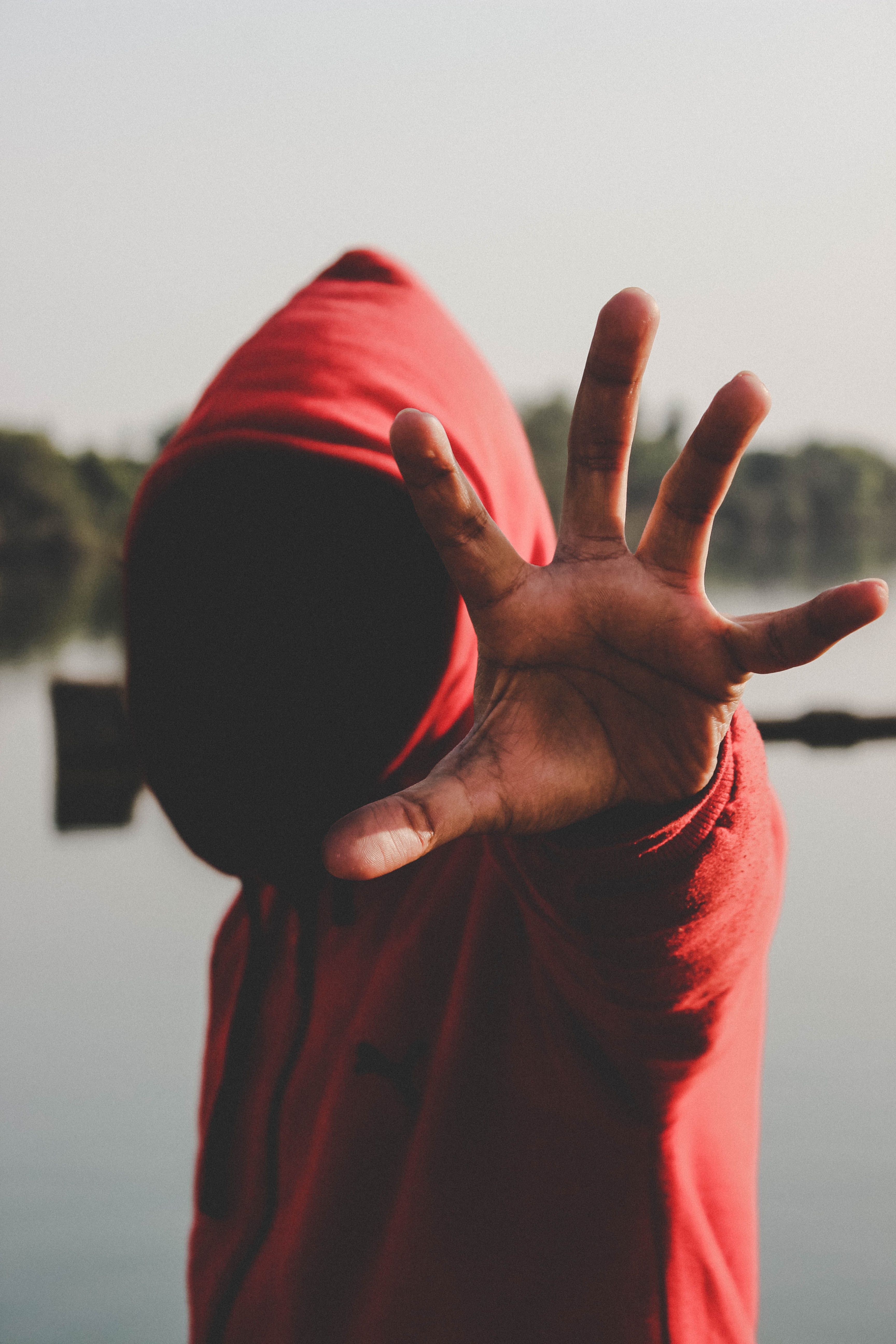 Black person with face obscured in shadow raises their hand to the camera